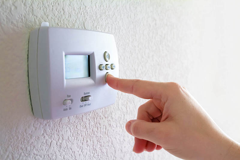 Hand pressing a button on a smart thermostat on a wall