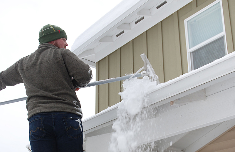 Man using a roof rake in winter.