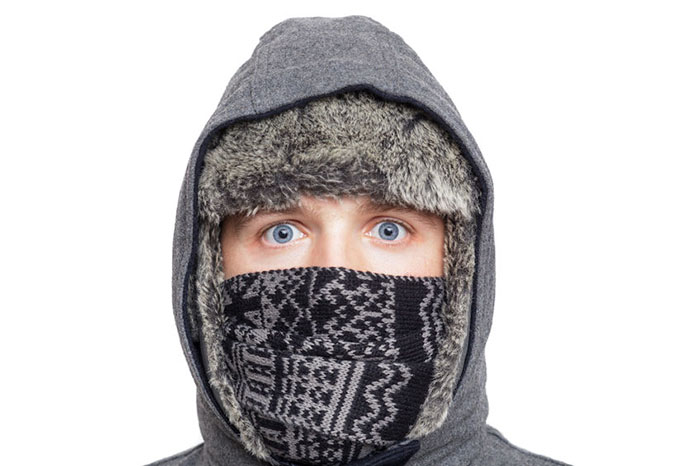 Young man in hat, scarf and hood hiding from the cold weather in